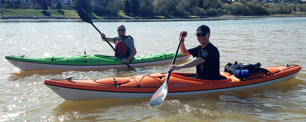 The Race | single blade or double blade paddle? Two kayakers paddling on a river during a sunny day.