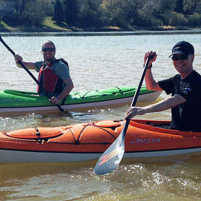 The Race | single blade or double blade paddle? Two kayakers paddling on a river during a sunny day.