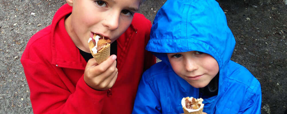 Two kids enjoying campfire cones while wearing colorful jackets outdoors.