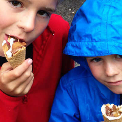 Two kids enjoying campfire cones while wearing colorful jackets outdoors.