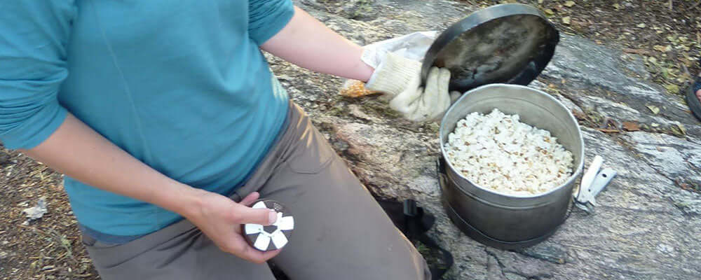 Camp popcorn being prepared in a pot by a person outdoors.