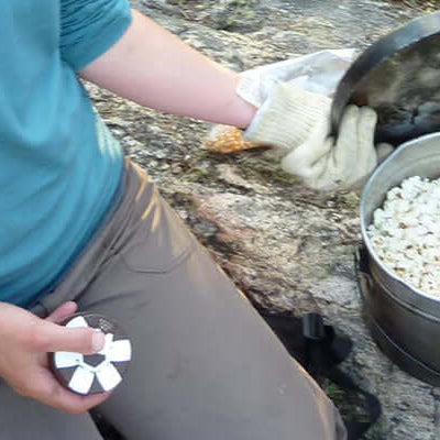 Camp popcorn being prepared in a pot by a person outdoors.