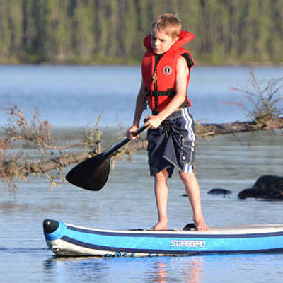 A boy in a life jacket paddle boarding on calm water, showcasing that paddle boarding anyone can do it.