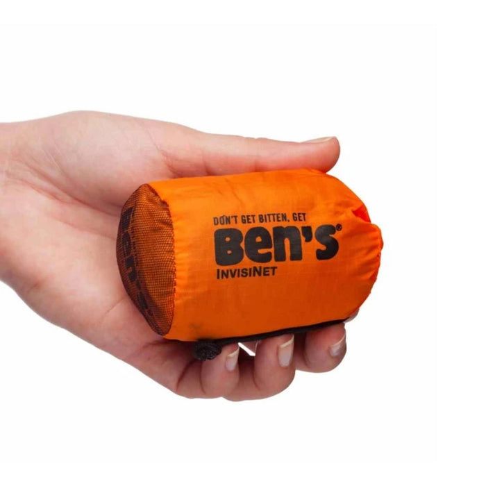 A hand holding a small orange rolled  pouch with black printed Ben's InvisiNet branding on a plain white background.