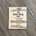 The Knot Tying Bible book by Colin Jarman, featuring a light wood-grain cover with three illustrated rope knots, placed on a gray wood-textured surface.