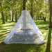A white mosquito net tent draped over a wooden picnic table in a sunlit park with green grass and trees.