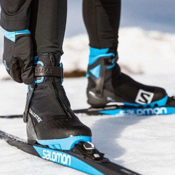 Close up of a person's black and blue ski boots and skis on a snowy background.