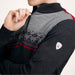A close-up of a man wearing a dark gray and gray heather knit sweater with a patterned yoke, red accents, and a small shield-shaped logo patch on the sleeve.