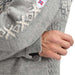 Close-up of a person wearing a gray knit sweater with cream Nordic-style patterns, a white shield patch with the Norwegian flag, and a black button closure.