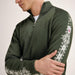 A man wearing an olive green knit quarter-zip sweater with white Nordic snowflake patterns on the sleeves, shown from the chest down against a light neutral background.