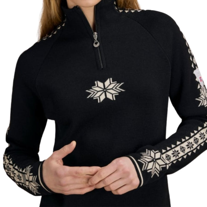 A close-up of a person wearing a black quarter-zip pullover sweater with white Fair Isle snowflake and geometric patterns on the chest and sleeves, set against a plain white background.