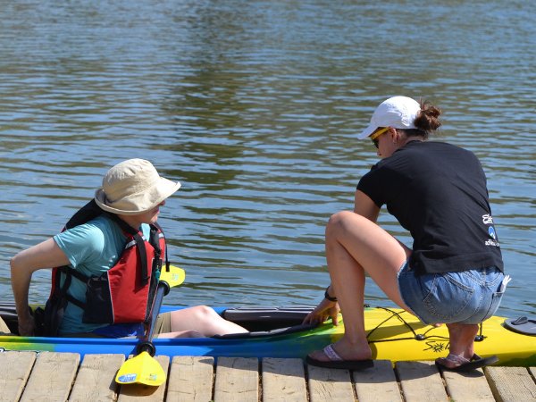 Two people preparing to kayak on a wooden dock by a body of water.