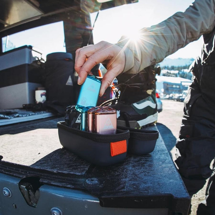 Person placing a blue metal hand warmer in a zip pod containing others with an outdoor parking lot in the background.
