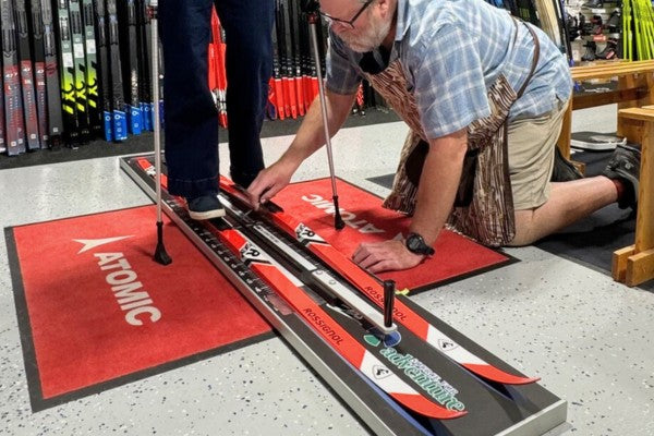 Person adjusting a ski on a ski fitting machine with 'Atomic' branding in the background.