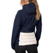 A woman seen from the back wearing a colorblock hooded jacket with a navy blue upper half and a cream quilted lower panel against a white studio background.
