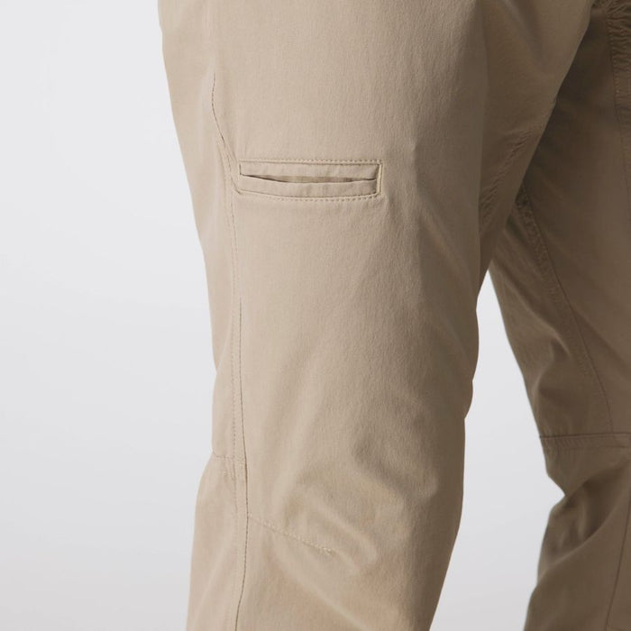 Close-up of a person's leg wearing beige cargo pants, showing a side pocket and the fabric texture against a light gray background.