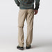 A person shown from the back wearing beige convertible pants, a green and yellow plaid long-sleeve shirt, and dark shoes against a light gray studio background.
