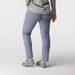 A person shown from the back wearing slim-fit trousers in a dusty periwinkle shade, paired with a light gray patterned shirt and blue-gray sneakers, against a plain light gray studio background.