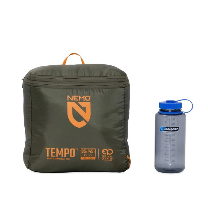 Packed sleeping bag cube beside a grey water bottle on a white background