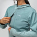 A close-up of a person wearing a light teal hooded jacket with a front zipper and a visible NRS logo on the chest, against a plain light gray background.