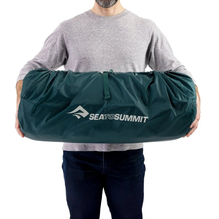 A person holding a dark green Sea to Summit mat across their torso, shown against a plain white background.