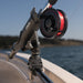 Close-up of a black fly fishing reel mounted on a rod holder on a boat, with red line spool and water in the background.