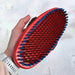 Red and blue bristle brush held by a person against a white background