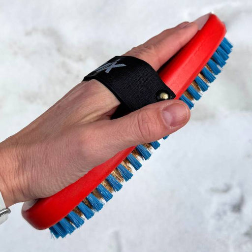 Hand holding a red and blue brush with a black strap against a white background