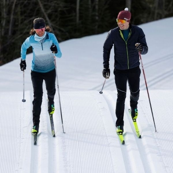 Two people skiing with black and blue clothing.