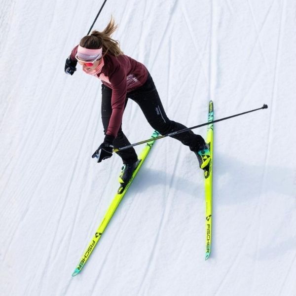 A woman with pink headband and dark clothing skiing on snow with bright yellow skis, seen from above.
