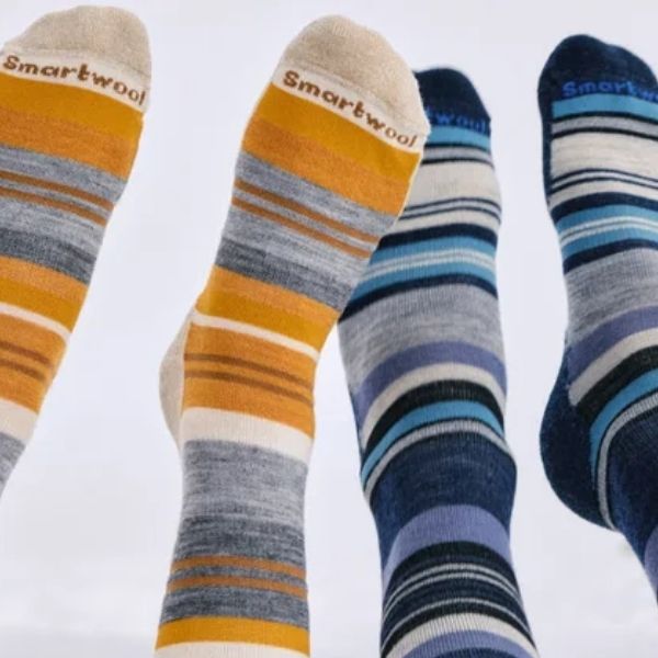 Four feet wearing striped colourful socks with Smartwool branding against a white background.