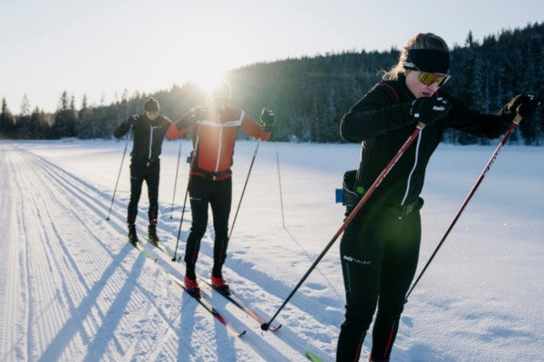 Three cross-country skiers on a snow-covered track with trees in the background