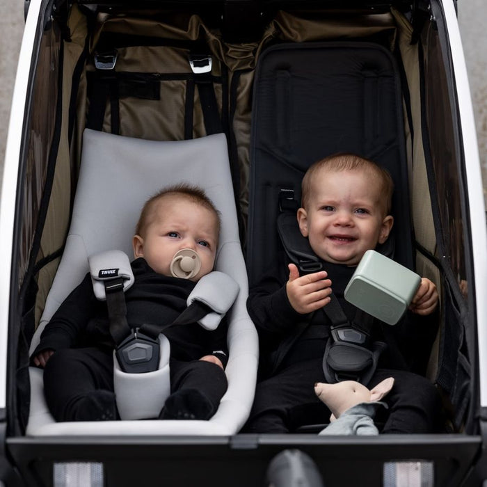 Two children in a stroller with one holding a toy and the other with a pacifier.