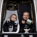 Two children in a stroller with one holding a toy and the other with a pacifier.