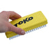 A hand holding a yellow TOKO plastic cleaning brush with white bristles against a plain white background.