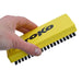 A hand holding a yellow TOKO horsehair brush with black bristles against a plain white background.