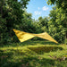 Yellow tarp set up in a forest clearing with trees and grass around.