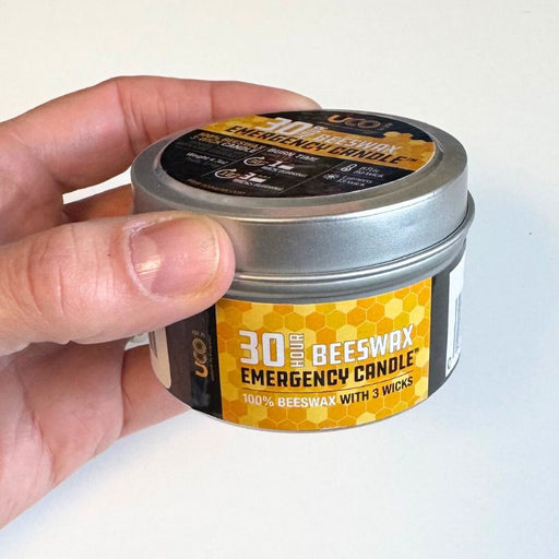Hand holding a 30-hour beeswax emergency candle in a metal tin with a yellow label.