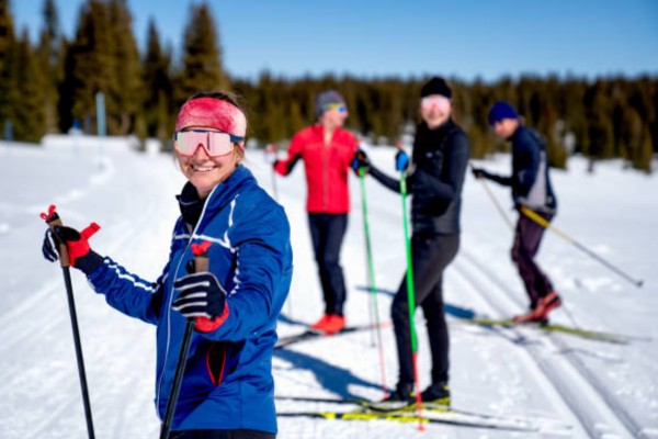 Group of people cross-country skiing on a snowy track with trees in the background.