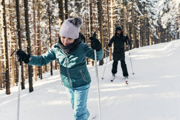 Two kids cross-country skiing in a snowy forest