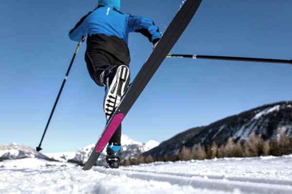 Person cross-country skiing on a snowy trail with mountains in the background
