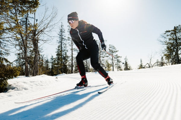 Person skate skiing on a snow-covered track with trees in the background